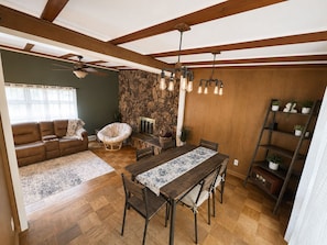 A dining area with a wooden table and chairs, a stone wall, and a ceiling fan.