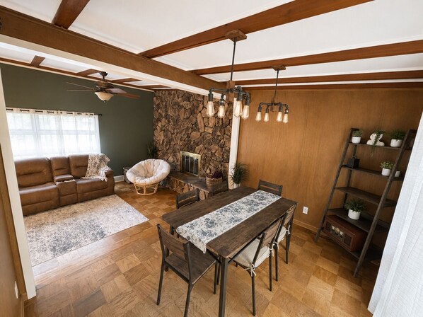 A dining area with a wooden table and chairs, a stone wall, and a ceiling fan.