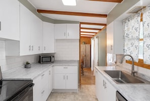 A modern kitchen with white cabinets, a microwave, a sink, and a wooden ceiling.