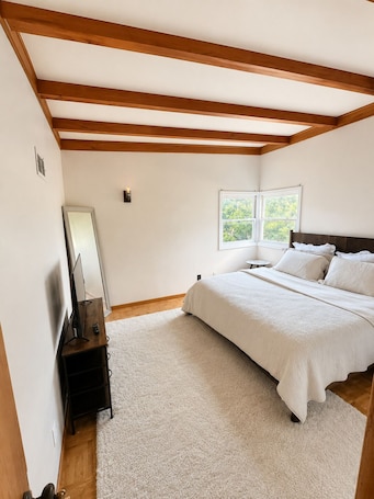 A bedroom with a bed, a TV, a window, and wooden beams on the ceiling.. 15 Mins to CWS - Charles Schwab Field!