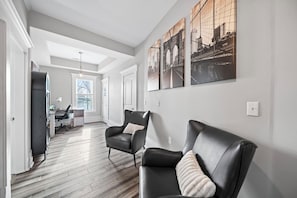 A modern interior with a wooden floor, a black leather sofa, a black leather armchair, and a desk with a lamp. - THE OAKWOOD!! Beautiful Historic 4BR Home Near Nationwide Children’s (Columbus)
