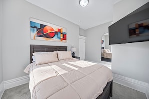 A bedroom with a bed, a nightstand, a wall-mounted abstract painting, a mirror, and a door. - THE OAKWOOD!! Beautiful Historic 4BR Home Near Nationwide Children’s (Columbus)
