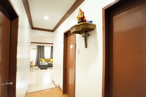 Ein Flur mit einer Holztür, einem an der Wand befestigten Regal mit einer Statue und einem Blick in einen Wohnbereich mit Sofa und Vorhängen.