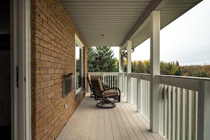 A covered porch with a brick wall, two wicker chairs, and a white railing.