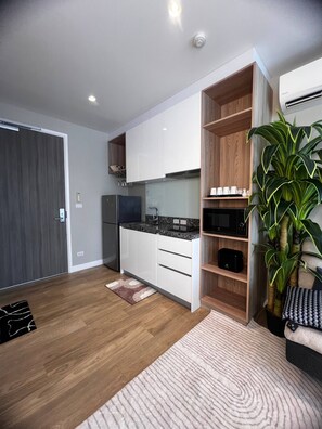 A modern kitchen with white cabinets, a built-in microwave, and a large potted plant. - Diamond Resort 1 bedroom (Tambon Choeng Thale)