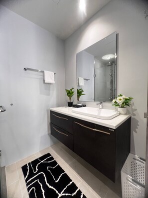 A modern bathroom with a white sink, dark cabinets, a large mirror, and a black and white rug. - Diamond Resort 1 bedroom (Tambon Choeng Thale)