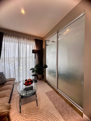 A modern living room with a sofa, a glass coffee table with fruit, a lamp, and a view through frosted glass doors. - Diamond Resort 1 bedroom (Tambon Choeng Thale)