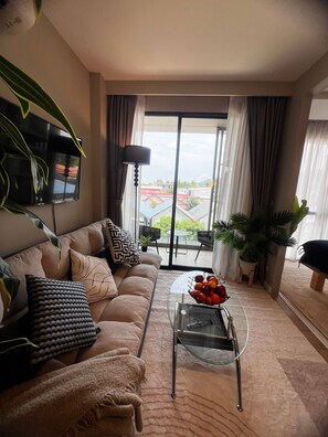 A living room with a sofa, a coffee table, a TV, and a view of the outside. - Diamond Resort 1 bedroom (Tambon Choeng Thale)