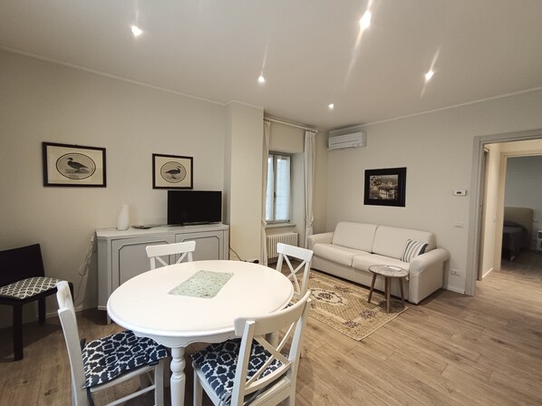 Una sala de estar con un sofá blanco, una mesa de comedor con sillas, un televisor y cuadros en la pared.