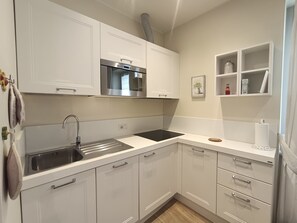 Una cocina moderna con armarios blancos, un lavamanos de acero inoxidable y un microondas integrado.