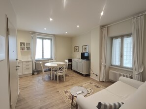 Una sala de estar moderna con un sofá blanco, una mesa de comedor con sillas, un televisor y un radiador.