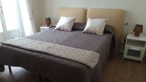 Una cama con una colcha estampada, dos almohadas, una lámpara de noche y una mesita de noche con lámpara.