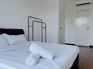 A neatly made bed with white linens and a rolled towel, a dark-colored headboard, a metal bed frame, and a white door with a handle. - Trival Lavender Homestay @ Sri Indah Sandakan (Sandakan)