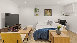 Uma sala moderna com televisão de tela plana, mesa de centro de madeira, sofá, cama com manta azul e escrivaninha com laptop.