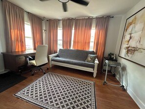 A room with a desk, chair, sofa, patterned rug, and a ceiling fan. - Family friendly 2-bedroom home in central FL close to I-4, Orlando & beaches! (DeLand)