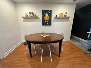 Un comedor con una mesa redonda, sillas y dos estantes en la pared con objetos decorativos.