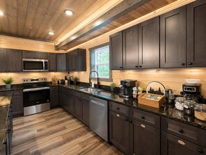 A modern kitchen with dark cabinets, stainless steel appliances, and a granite countertop. - Luxury Group Retreat Gatlinburg with Indoor Pool, Hot Tub, Theatre, Pickle Ball (Pigeon Forge)