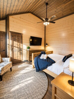 A wooden cabin-style room with a bed, a desk, a chair, a television, and a ceiling fan. - Luxury Group Retreat Gatlinburg with Indoor Pool, Hot Tub, Theatre, Pickle Ball (Pigeon Forge)
