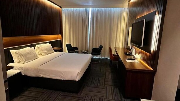 A hotel room with a large bed, a desk with a flat-screen TV, a chair, and a TV on the wall. - Raha Grand Hotel (Dubai)