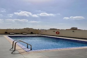 Ein Pool auf dem Dach mit einer Metallleiter, umgeben von einer niedrigen Mauer und einem wolkenlosen Himmel.