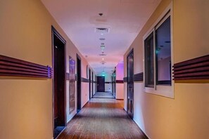 Ein langer, schmaler Hotelgang mit Türen an beiden Seiten, eingelassener Beleuchtung und einem gemusterten Teppich.