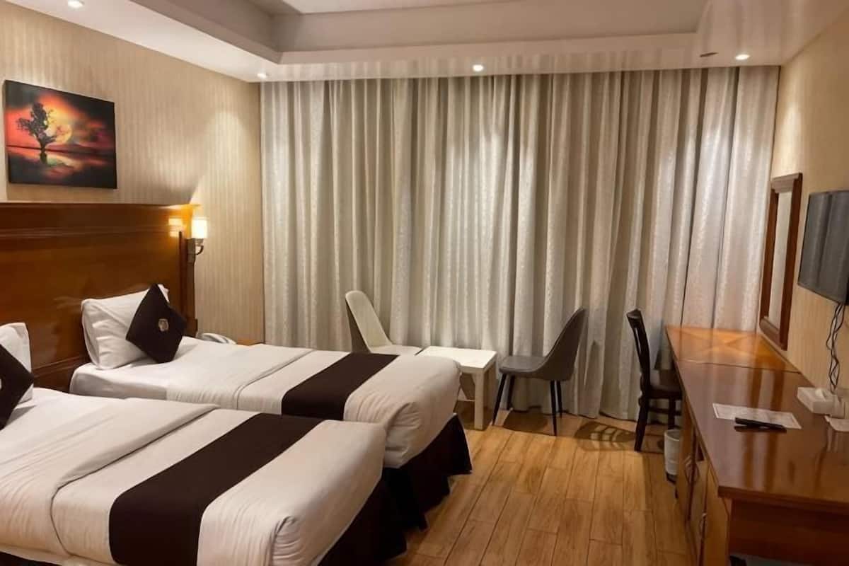 A hotel room with two beds, a desk, a chair, a TV, and a large window with curtains.