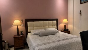 Een slaapkamer met een bed, twee nachtkastjes met lampen, een wandairconditioner en een schilderij aan de muur.