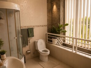 A bathroom with a shower, toilet, and a window with a balcony. - Griyaku Homestay (Badung)