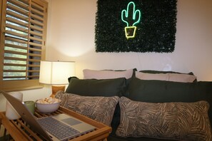 Una stanza con un portatile su un tavolo di legno, un recipiente con popcorn, un cartello luminoso a neon a forma di cactus e un divano con cuscini decorati.