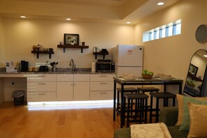 Una cucina moderna con mobili bianchi, un forno a microonde e un frigorifero. C'è un'area pranzo con un tavolo e sedie, e una piccola finestra sopra il lavello.