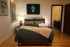 Een slaapkamer met een bed, nachtkastjes, een lamp, een wanddecoratie van een cactus, een spiegel en een houten vloer.