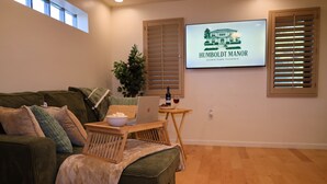 Ein Wohnzimmer mit einer Couch, einem Laptop auf einem kleinen Tisch, einer Schüssel Popcorn und einem Fernseher, der 'HUMBOLDT MANOR DOWNTOWN PHOENIX' anzeigt.