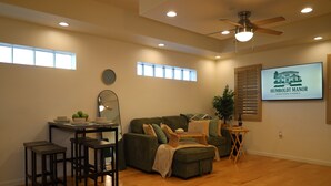 Ein Wohnzimmer mit einer Couch, einem Couchtisch, einem Esstisch mit Hocker, einem Deckenventilator und einem Fernseher, der 'HUMBOLDT MANOR DOWNTOWN PHOENIX' zeigt.