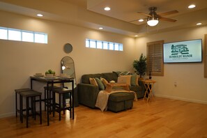 Een woonkamer met een bank, een salontafel, een eettafel met krukken, een plafondventilator en een televisie waarop 'HUMBOLDT MANOR DOWNTOWN PHOENIX' staat.