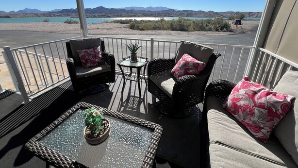 A covered outdoor seating area with wicker furniture, a glass table, and a potted plant. - Relaxing 2 Bedroom with Panoramic Lake View from inside and out (Lake Havasu City)