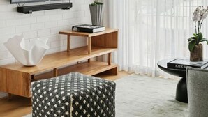 Uma sala de estar moderna com televisão de tela plana, estantes de madeira, um banquinho acolchoado e um ventilador de teto.
