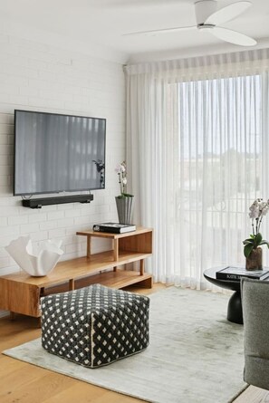 Een moderne woonkamer met een flatscreen televisie, houten planken, een comfortabele poef en een plafondventilator.