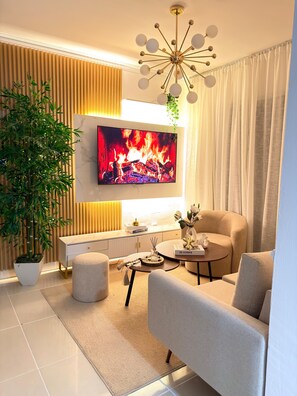 Ein modernes Wohnzimmer mit Flachbildfernseher, einer Couch, einem Couchtisch, einer Topfpflanze und einer dekorativen Deckenleuchte.
