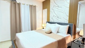 Quarto de hotel moderno com uma cama grande, uma mesa de cabeceira com abajur, criado-mudo e um espelho.