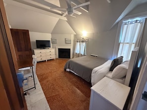 Ein Schlafzimmer mit Bett, Schminktisch, Fernseher, Kamin und Deckenventilator.