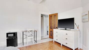 A bedroom with a television on a dresser, a microwave, a chair, and a door leading to another room.