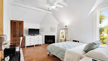 A bedroom with a bed, a television, a fireplace, and a ceiling fan.