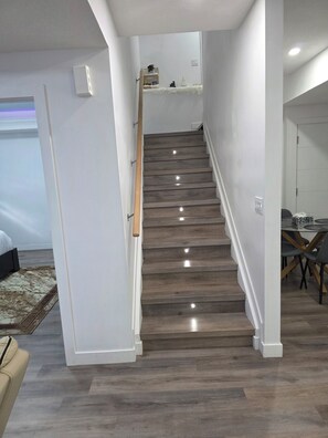 Una scala con gradini in legno e pareti bianche, che conduce a una piattaforma con uno scaffale e un tavolino.