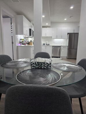 Un'area pranzo moderna con un tavolo in vetro, sedie rivestite di grigio e un runner da tavolo decorato.