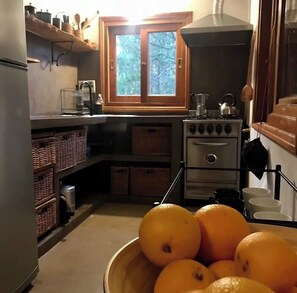 A compact kitchen with a stove, a window, and baskets on the shelves. - Stone house next to the El Durazno River on private property (Villa Yacanto)