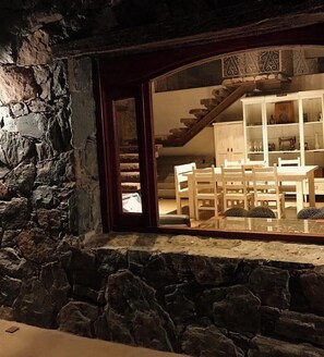 A stone wall, a wooden staircase, and a dining area with white furniture. - Stone house next to the El Durazno River on private property (Villa Yacanto)