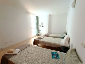 Hotellihuone, jossa on kaksi sänkyä, ikkuna, jossa on verhot, pieni pöytä ja seinälle kiinnitetty peili.