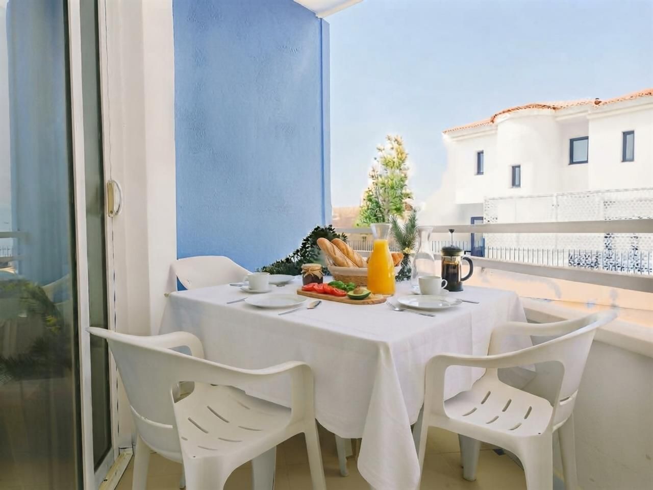 Een balkon met een ontbijtje aan tafel, inclusief brood, fruit en een drankje.