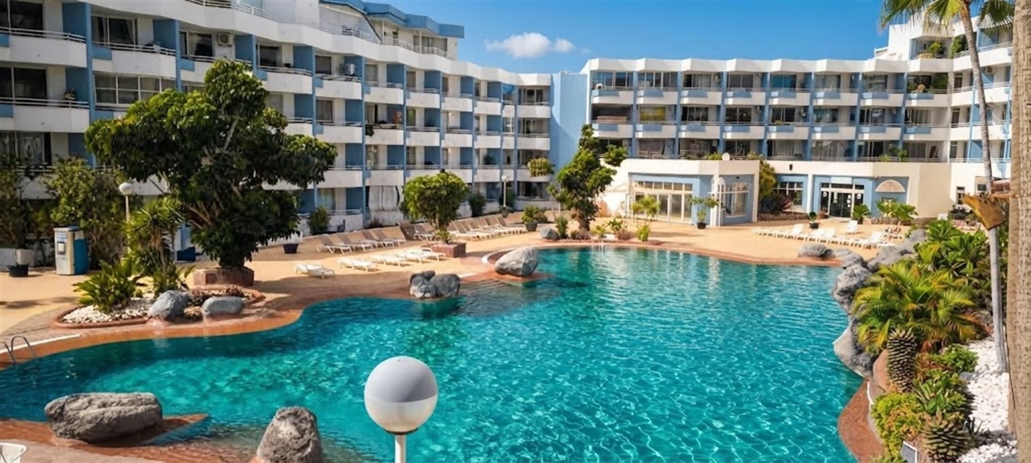 Ein Hotel mit Swimmingpool, Liegestühlen und Palmen.
