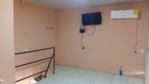 A room with a TV mounted on the wall, an air conditioner, and a metal railing. - Downtown 2-story Tiny House (Granada)